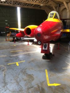 A red and yellow aeroplane on display in a hangar, with yellow directional arrows on the floor.