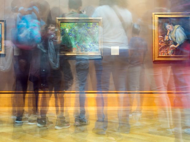 Long exposure image of many people standing in front of paintings in a gallery