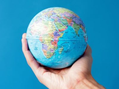 A hand holds a small planet earth globe