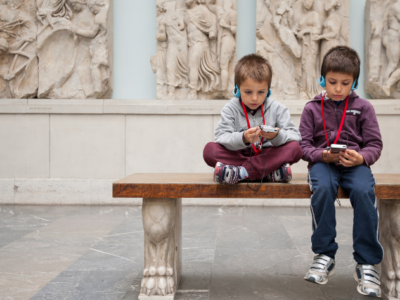 Two young boys in school uniform are sitting on a bench in a music whilst listening to audio guides.