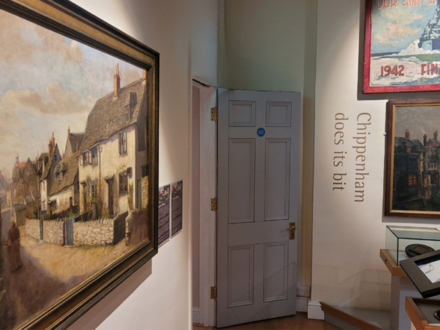 A painting of a cottage hanging on a gallery wall