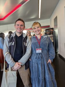 A man and a woman standing next to each other smiling at a conference